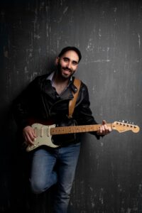 Músico con guitarra eléctrica sonriendo en un fondo oscuro