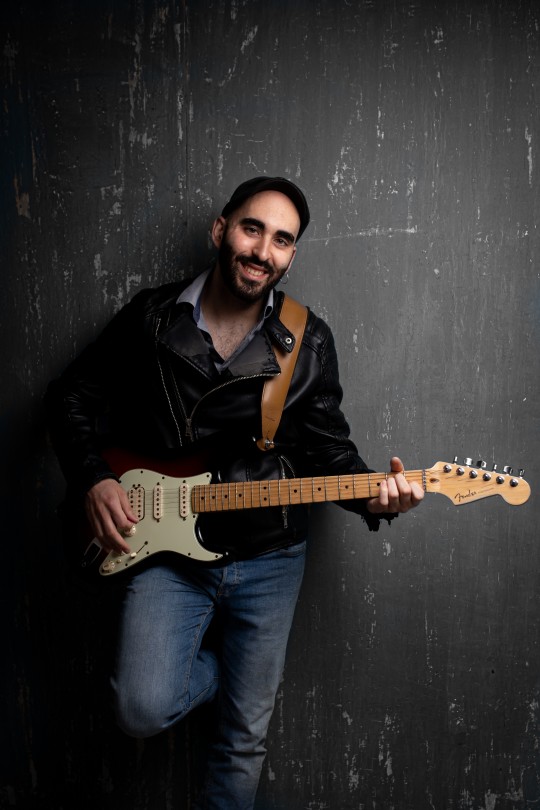 Músico con guitarra eléctrica sonriendo en un fondo oscuro