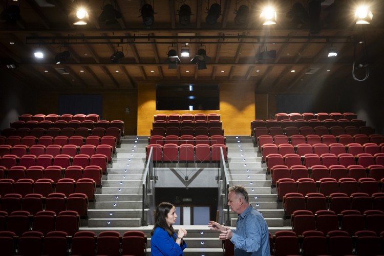 Dos personas conversando en un teatro con asientos rojos vacíos