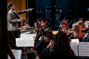 Director de orquesta señalando a jóvenes músicos en un concierto