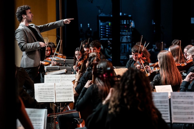 Director de orquesta señalando a jóvenes músicos en un concierto
