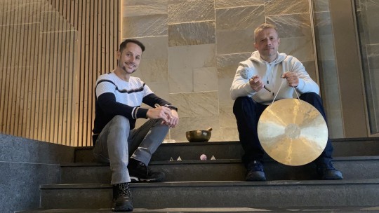 Dos hombres sentados en escaleras con instrumentos de sanación